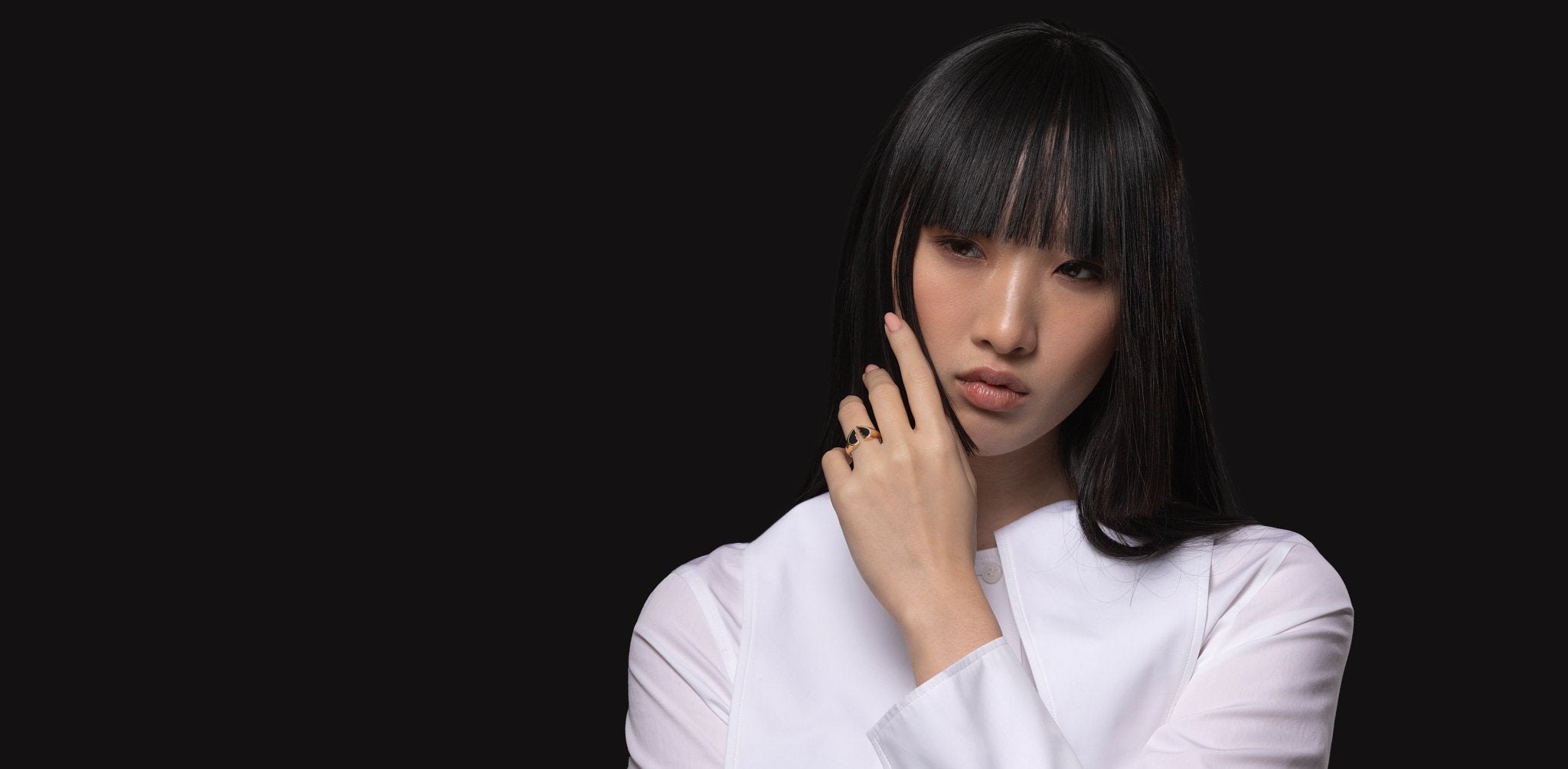 A female model wearing a white suit, a Broken Promise Yellow Gold Black Ceramic Ring on her finger.